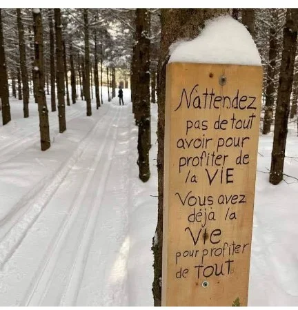 Panneau de bois portant une citation dans un sentier enneigé près de la yourte